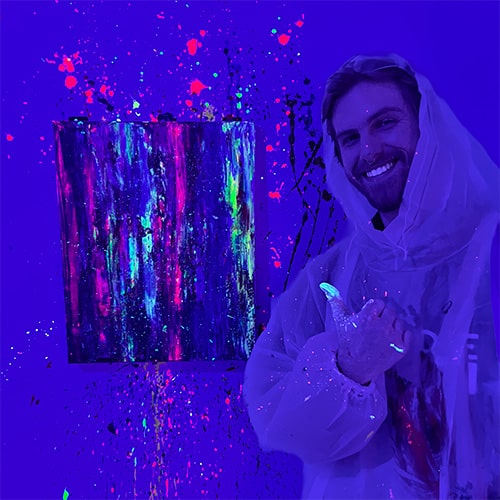 A man smiling and giving a thumbs up next to his painting in UV light